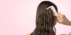 Rückansicht einer jungen Frau mit nassen Haaren, die sich mit einem grobzinkigen Kamm ihr langes Haar kämmt als Sinnbild für Tipps zum Haare kämmen